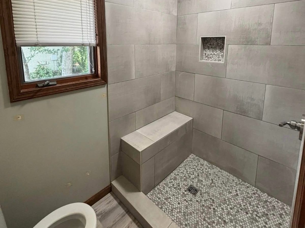 After: grey tile walk-in shower with a built-in bench, niche and pebble floor